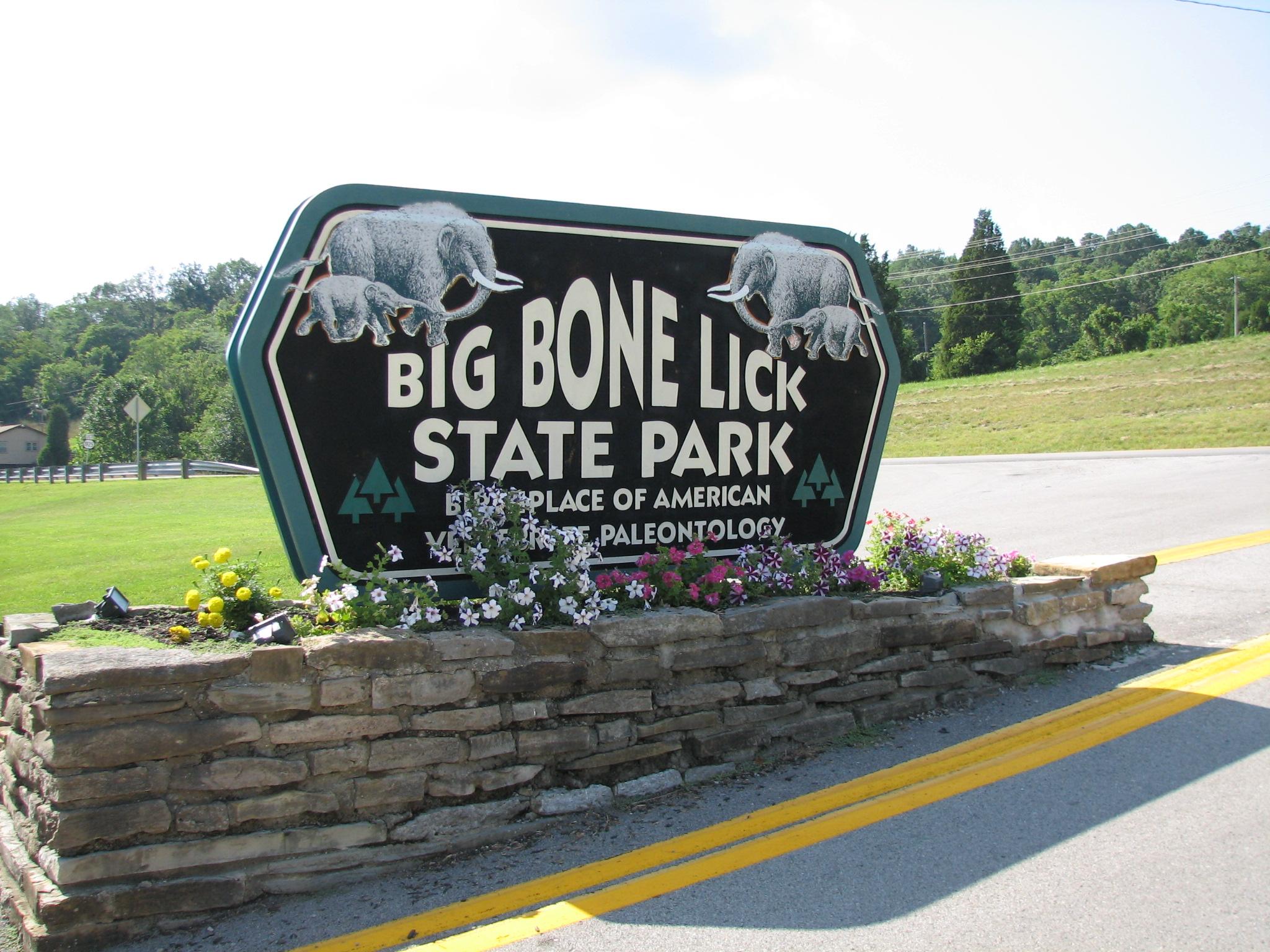 Carved park entry sign with mammoth silhouettes flanked by flowering planters at Big Bone Lick State Park.