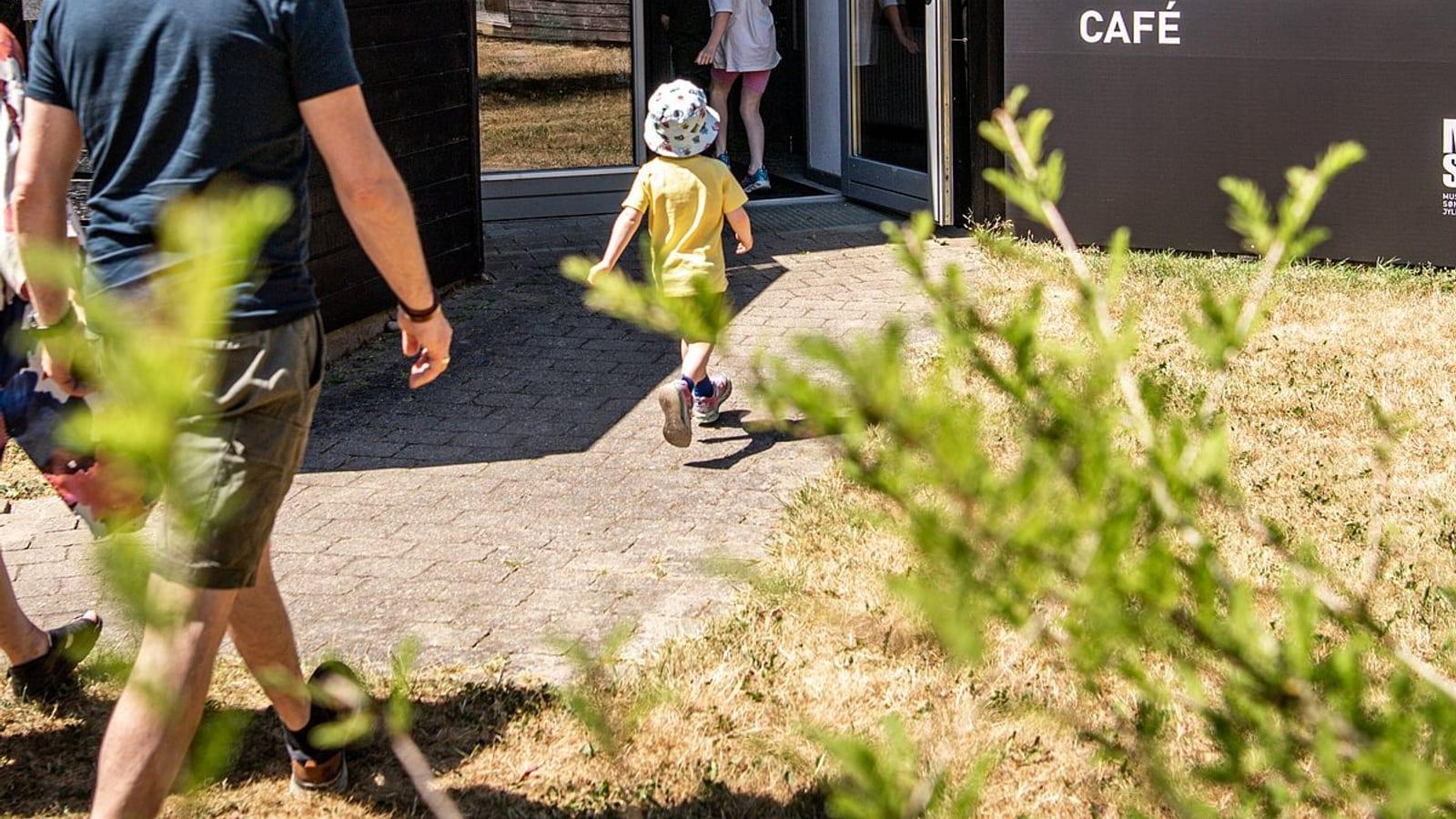 Child running toward the café entrance at the Gram Clay Pit visitor area on a sunny day in southern Denmark.
