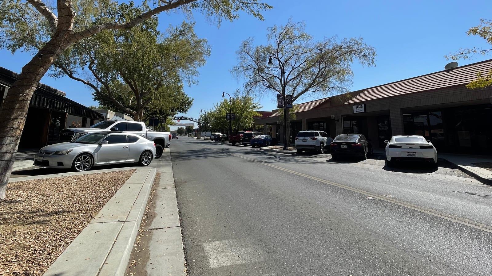 Small-town street lined with leafy trees and low storefronts on a sunny day in downtown Coalinga, California.