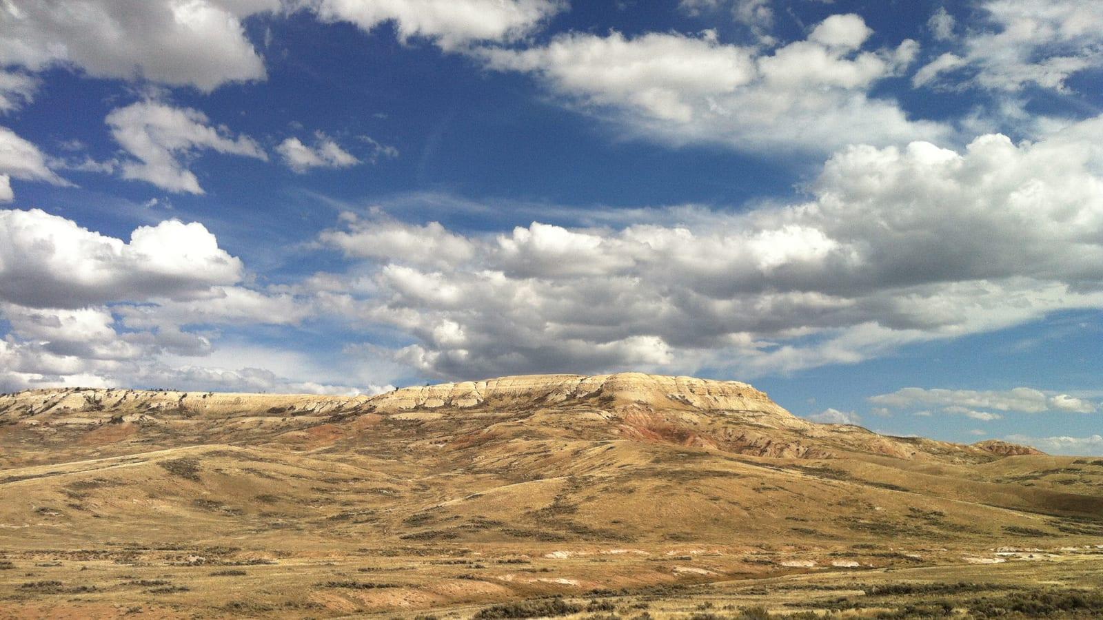 Wide prairie with golden grass and a long pale-capped ridge under a partly cloudy sky near Kemmerer, Wyoming.